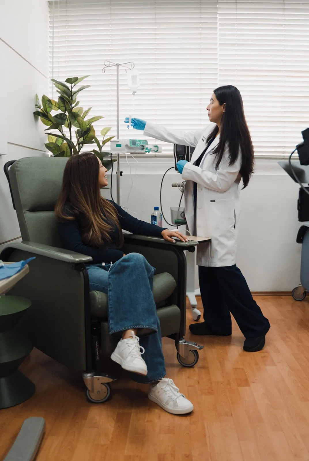 A patient seated in an infusion chair while a Celva clinician adjusts the IV line
