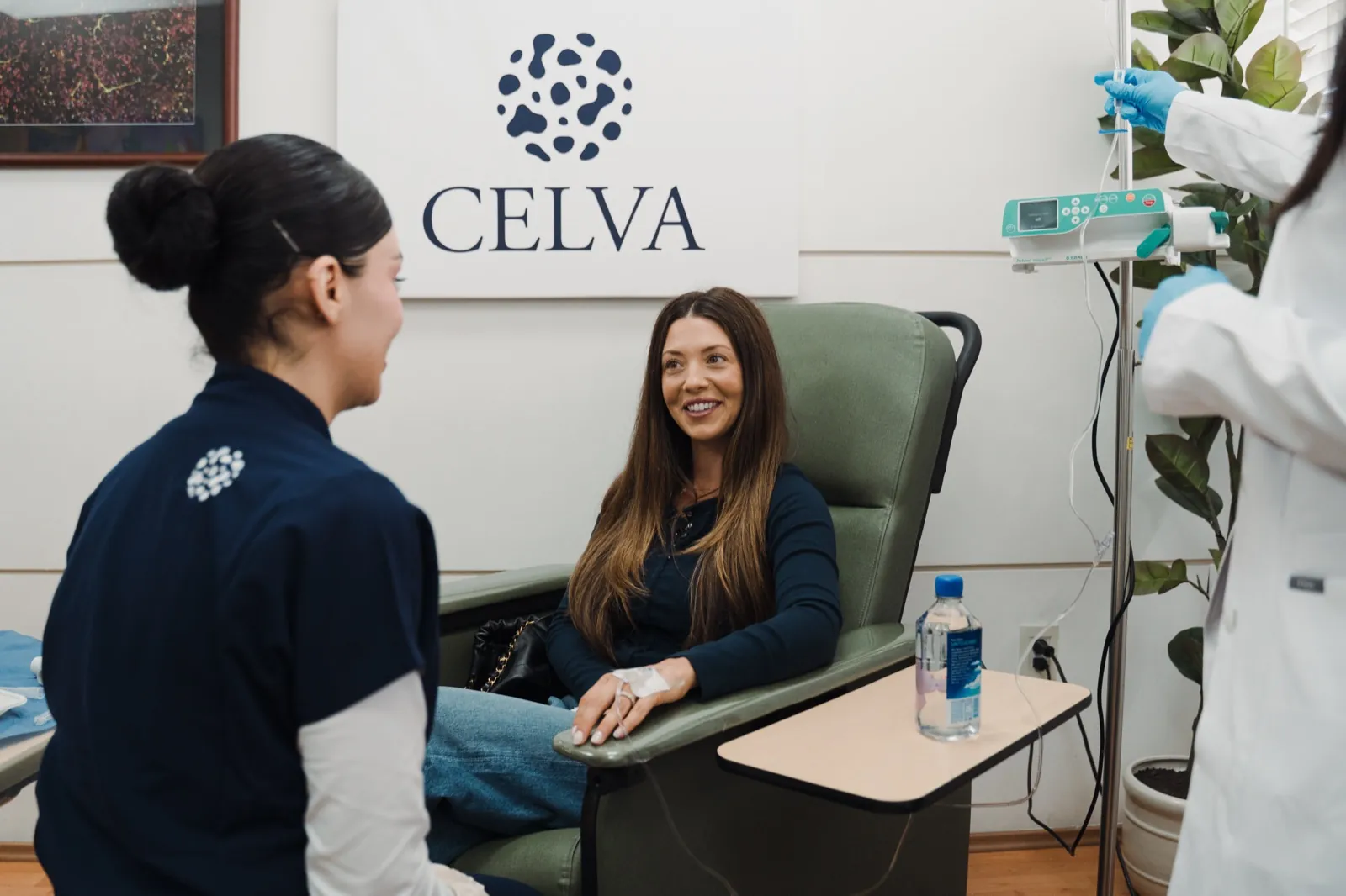 A patient seated in the private suite recliner with a Celva clinician and an IV pump beside her